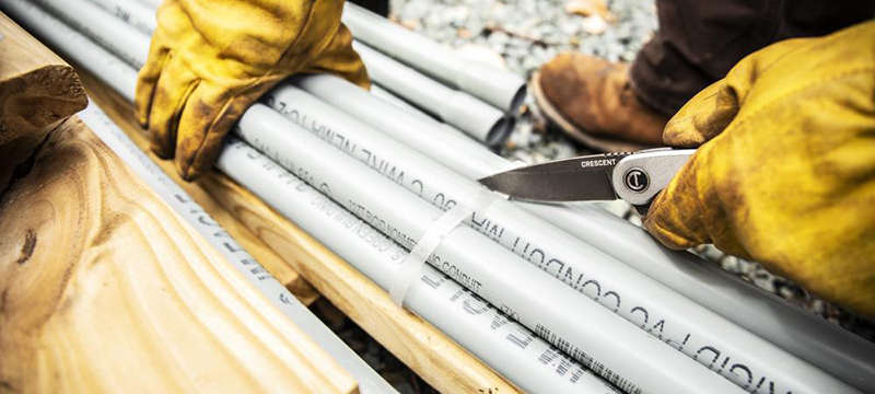 A construction worker cuts a bundle using a Crescent three and a quarter inch drop point aluminum handle pocket knife